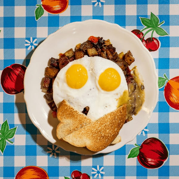 Doo-Dah Diner's breakfast plate with two fried eggs, hash, gravy, and toast on a checkered tablecloth.
